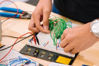 A student's hands are working on building or manipulating some type of wired device.