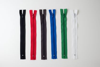 six zips laid flat on a table, each a different color: grey, red, black, blue, green and white