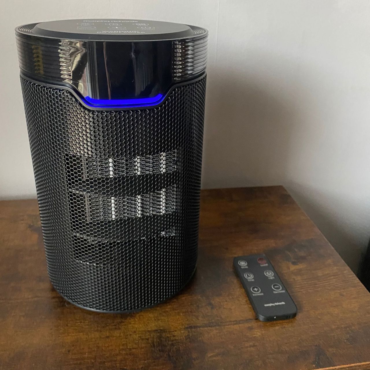 Morphy Richards HeatFlux 1.5kW Ceramic Fan Heater in cool mode on a wooden surface with the remote control by the side