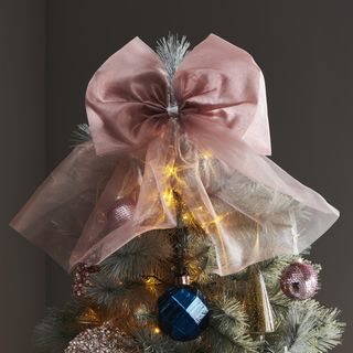 A pink satin and organza bow-shaped Christmas tree topper on artificial Christmas tree