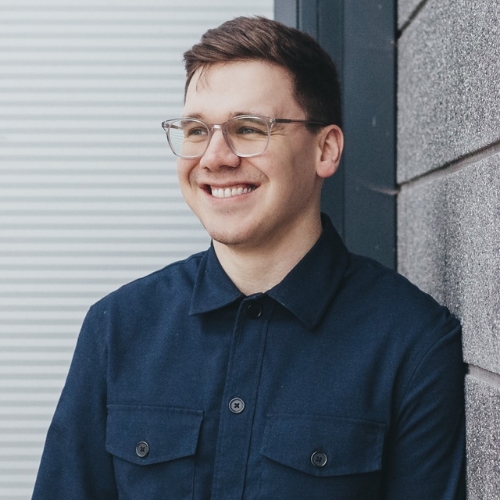 Image of James Mellan-Matulewicz, a man with short brown hair and glasses wearing a navy blue button-down shirt.