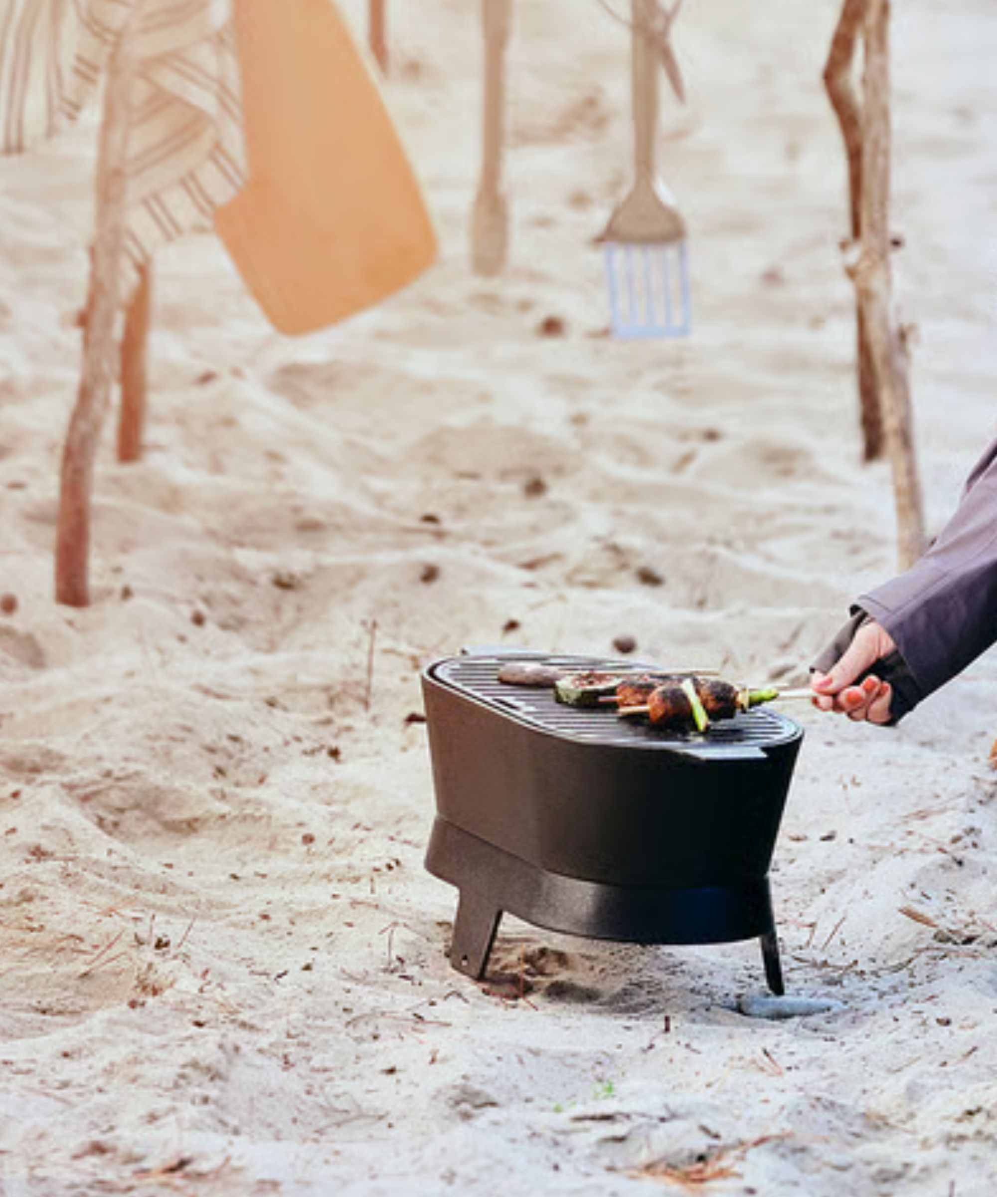 A small black cast iron gill on sand, with some vegetables on it.