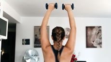 A woman pressing two dumbbells overhead during a home workout 