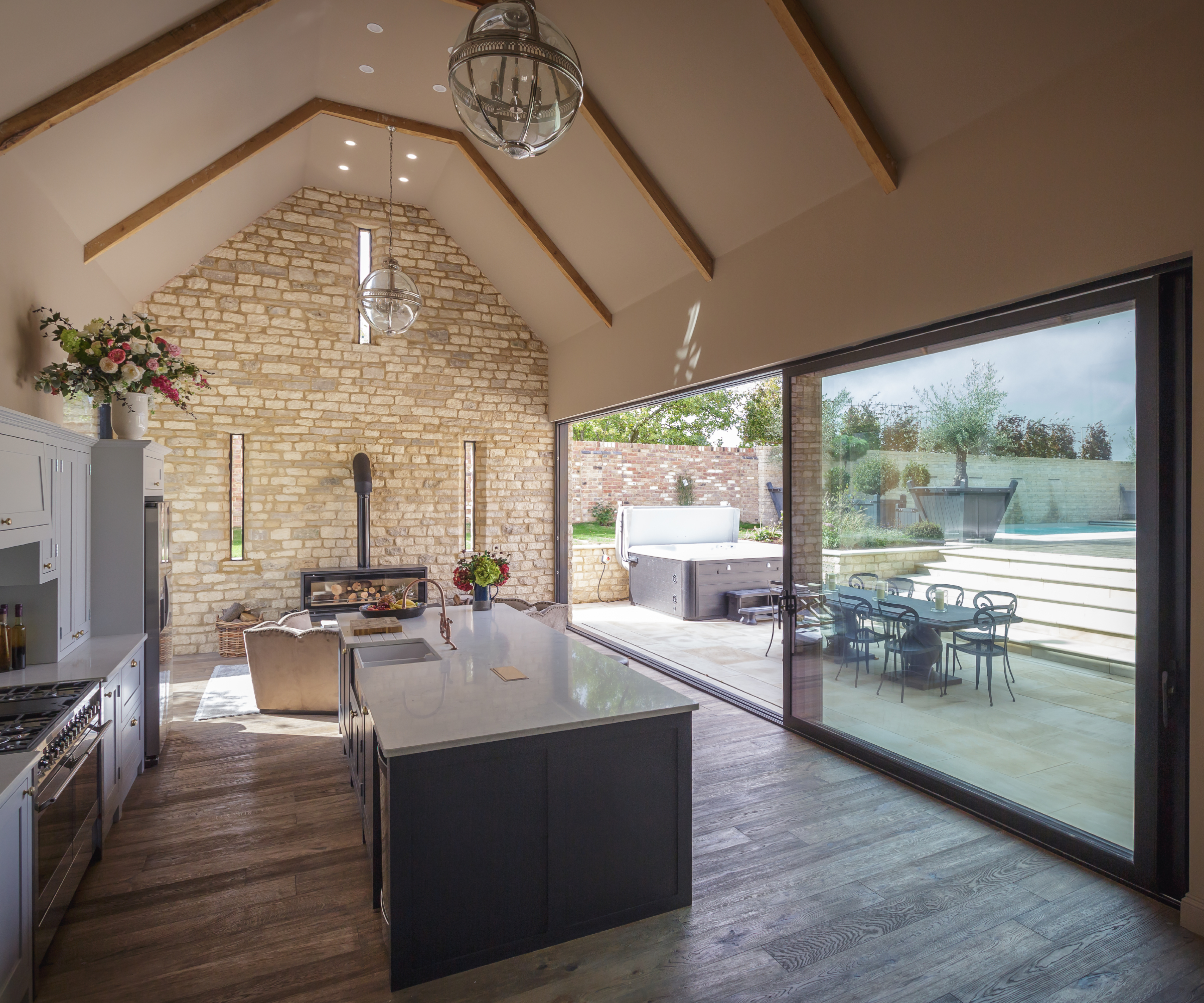 inside of open plan kitchen living room in barn with double height ceiling, wooden beams inset into ceiling and large sliding doors leading topatio