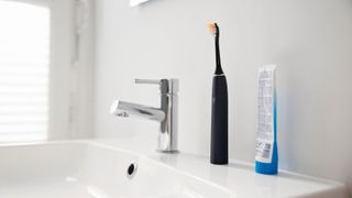 Sensitive teeth toothbrush sitting on side of sink with a tube of toothpaste