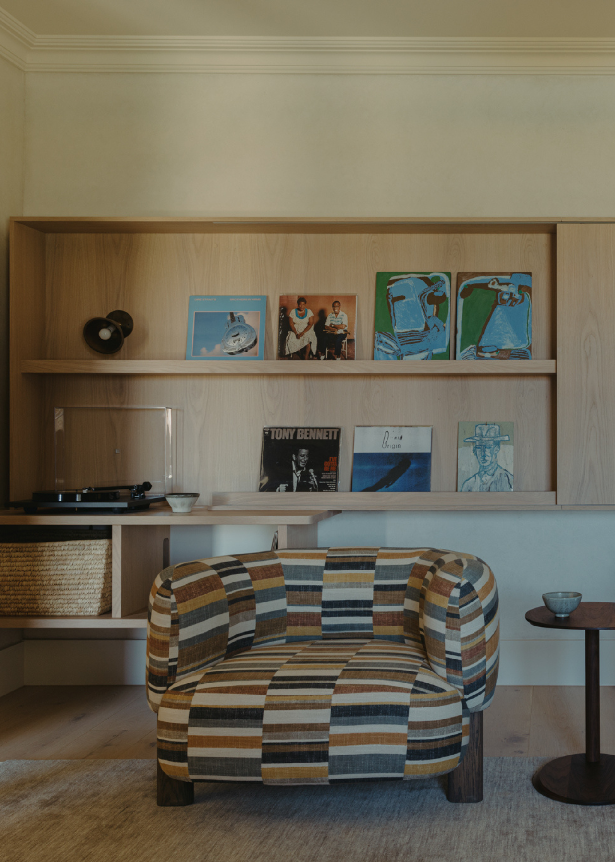A listening room with a patchwork armchair, a side table, a record player, and a wall of vinyl