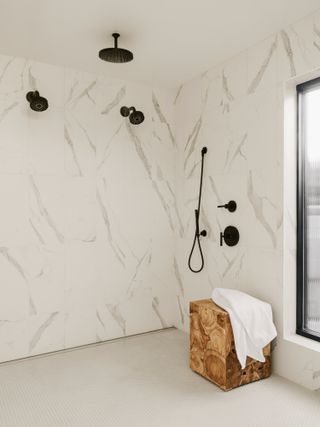 Porcelain tile-clad wet room with matt black shower fixtures and burl wood stool