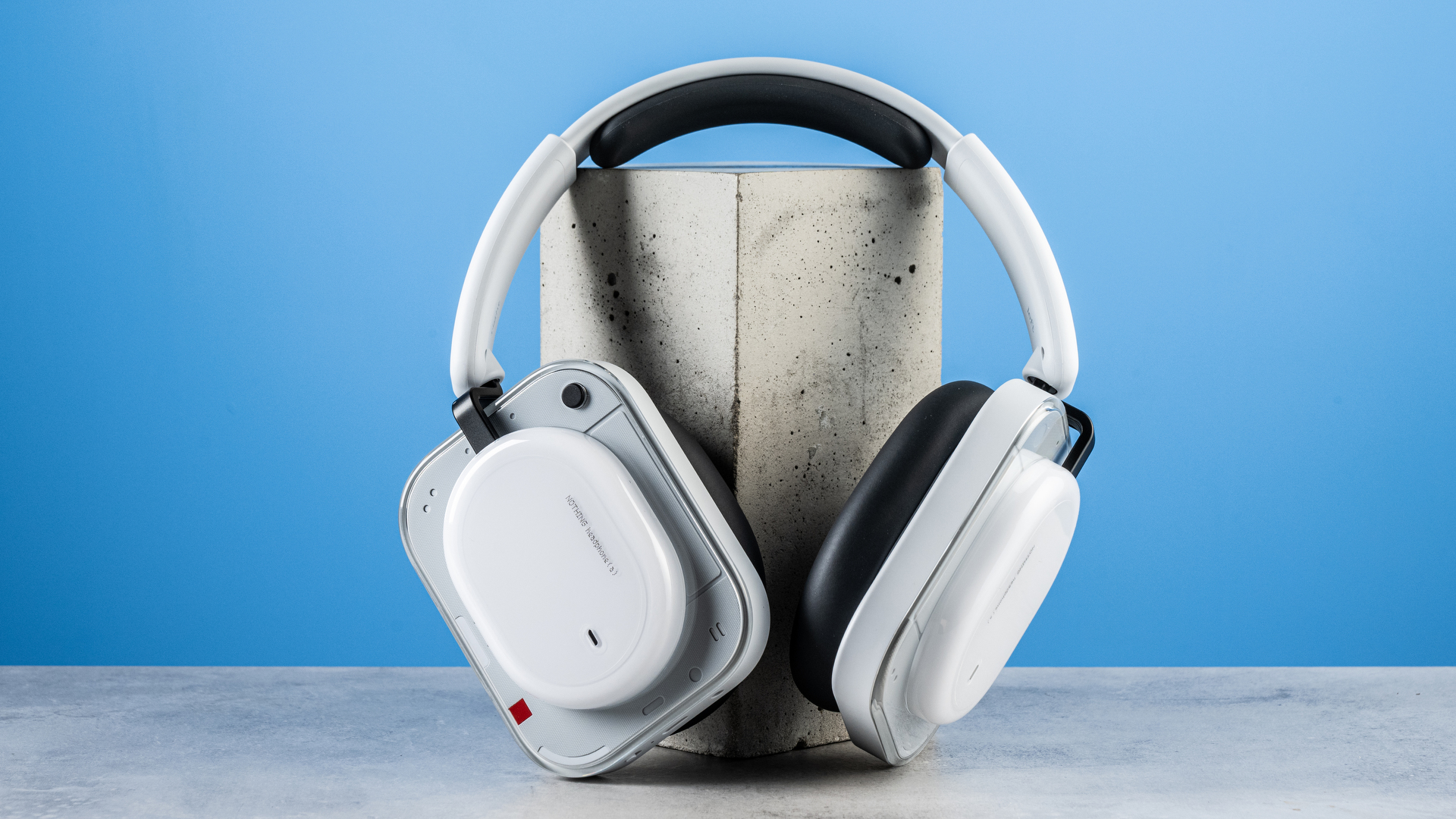 the nothing headphone (a) photographed against the blue tom's guide background, showing the transparent and white ear cups with red accents, the padded headband, and the accessories including 3.5mm jack