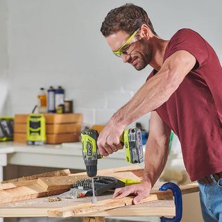 Man using Ryobi drill to drill wood in workshop