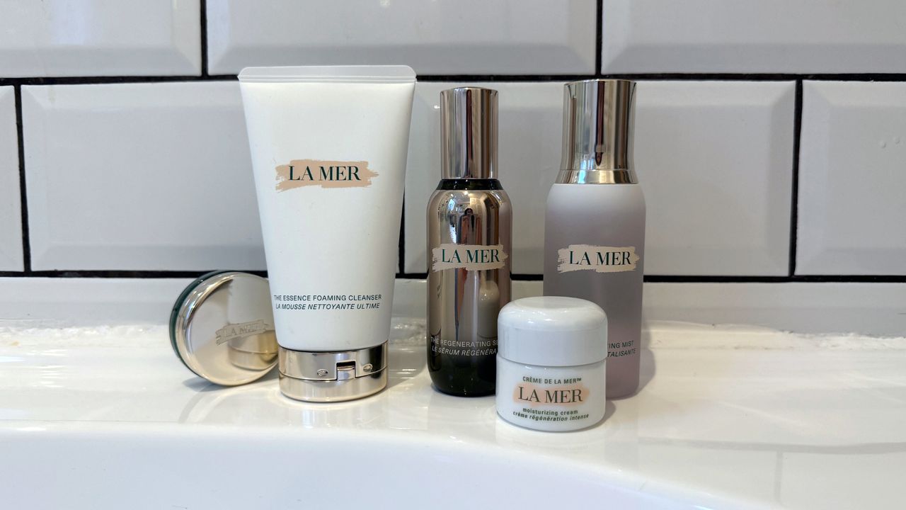 A selection of the best La Mer products featured in this guide, stood on the side of a white bathtub in front of a white tiled background