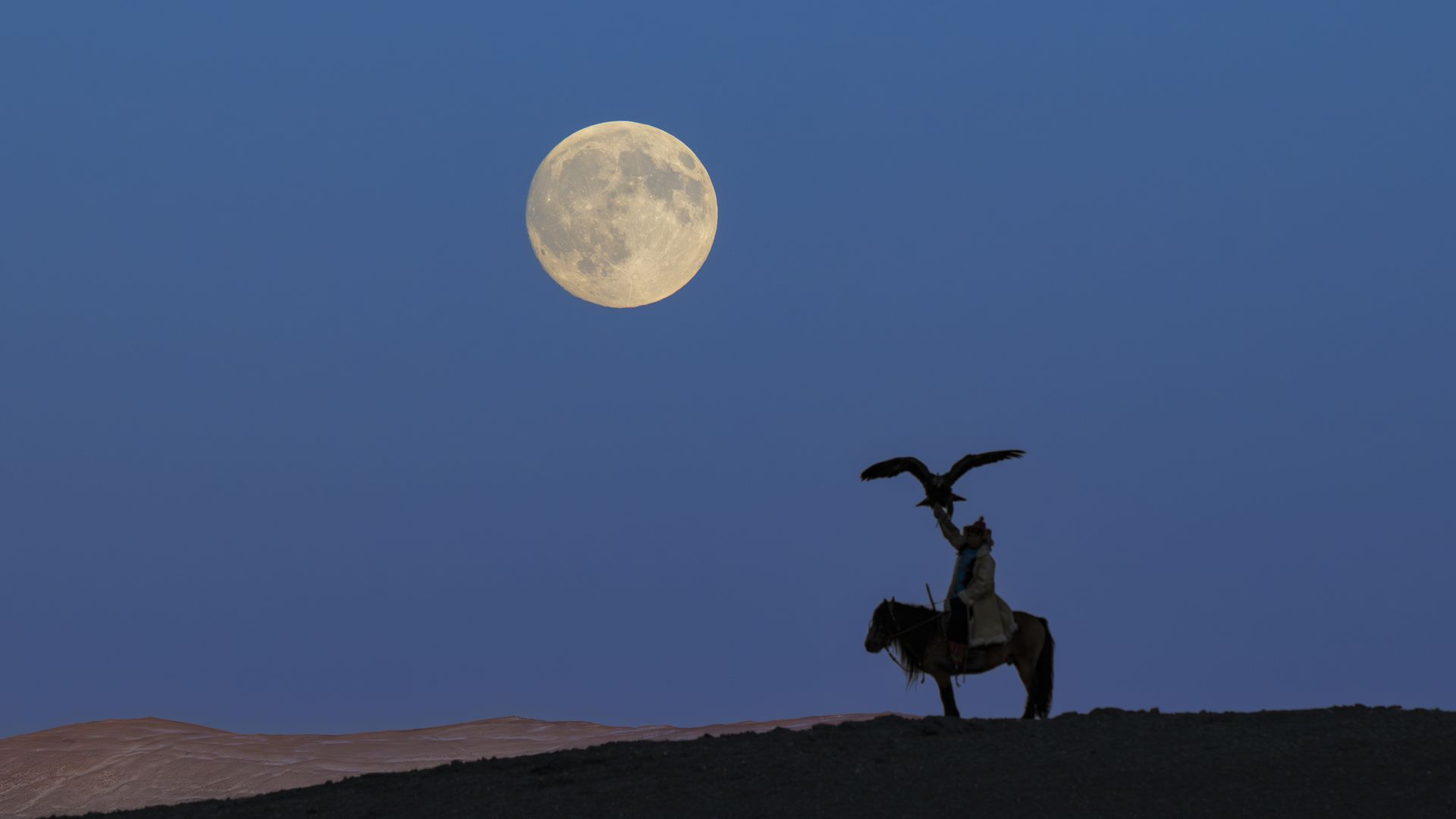 a large full moon in the sky, a man riding a horse holds up an eagle to the sky.