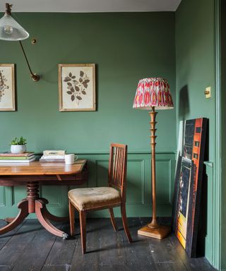 Living room with green walls, dark flooring with red rug, wooden table and chair.