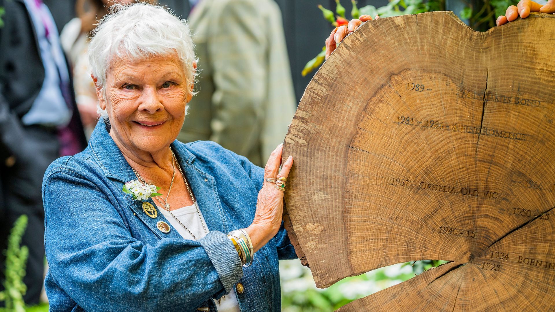 Judi Dench at the 2022 RHS Chelsea Flower Show posing with the carving of an oak timber round with key dates from her life and career
