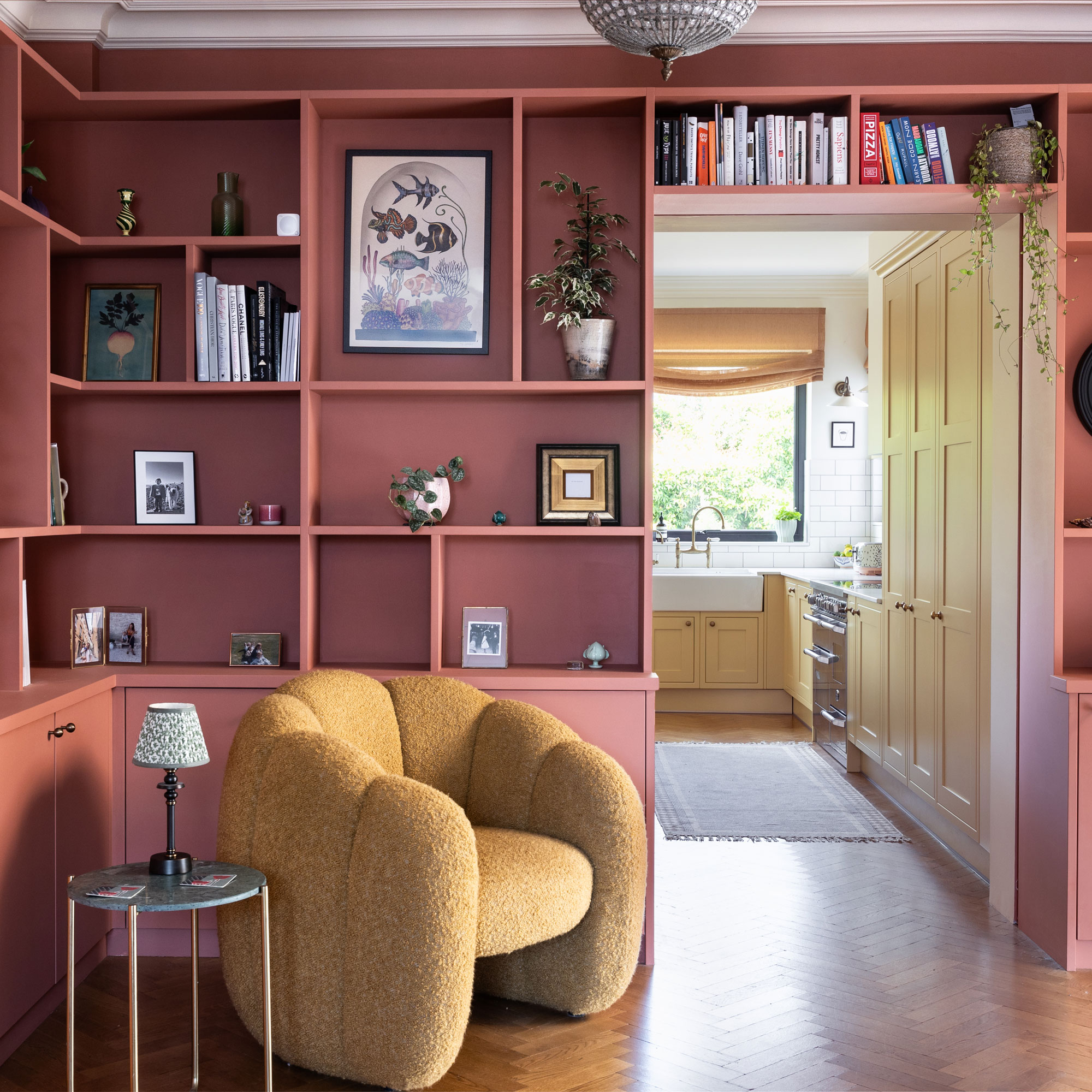 Built in shelving painted pink with a yellow scalloped armchair and a side table with rechargeable table lamp