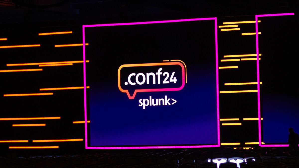 The Splunk .conf24 logo on a keynote screen live at Splunk .conf24 in Las Vegas. Decorative: The scene is lit in neon purple and orange lighting.