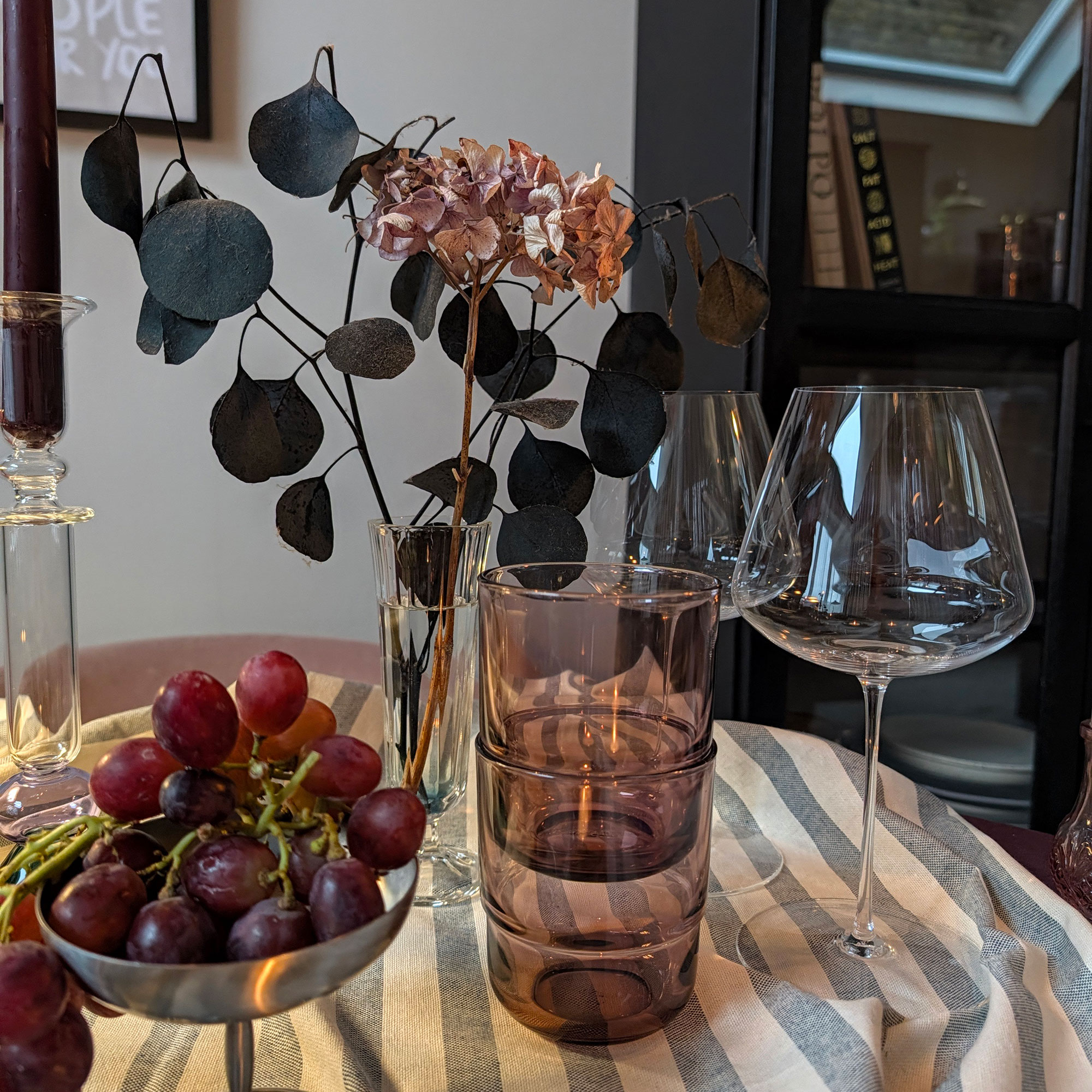 Two purple nesting glass tumblers beside wine glasses on striped tablecloth