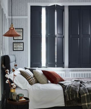 A white bedroom with black bed, large grey shutters on the inside of the windows