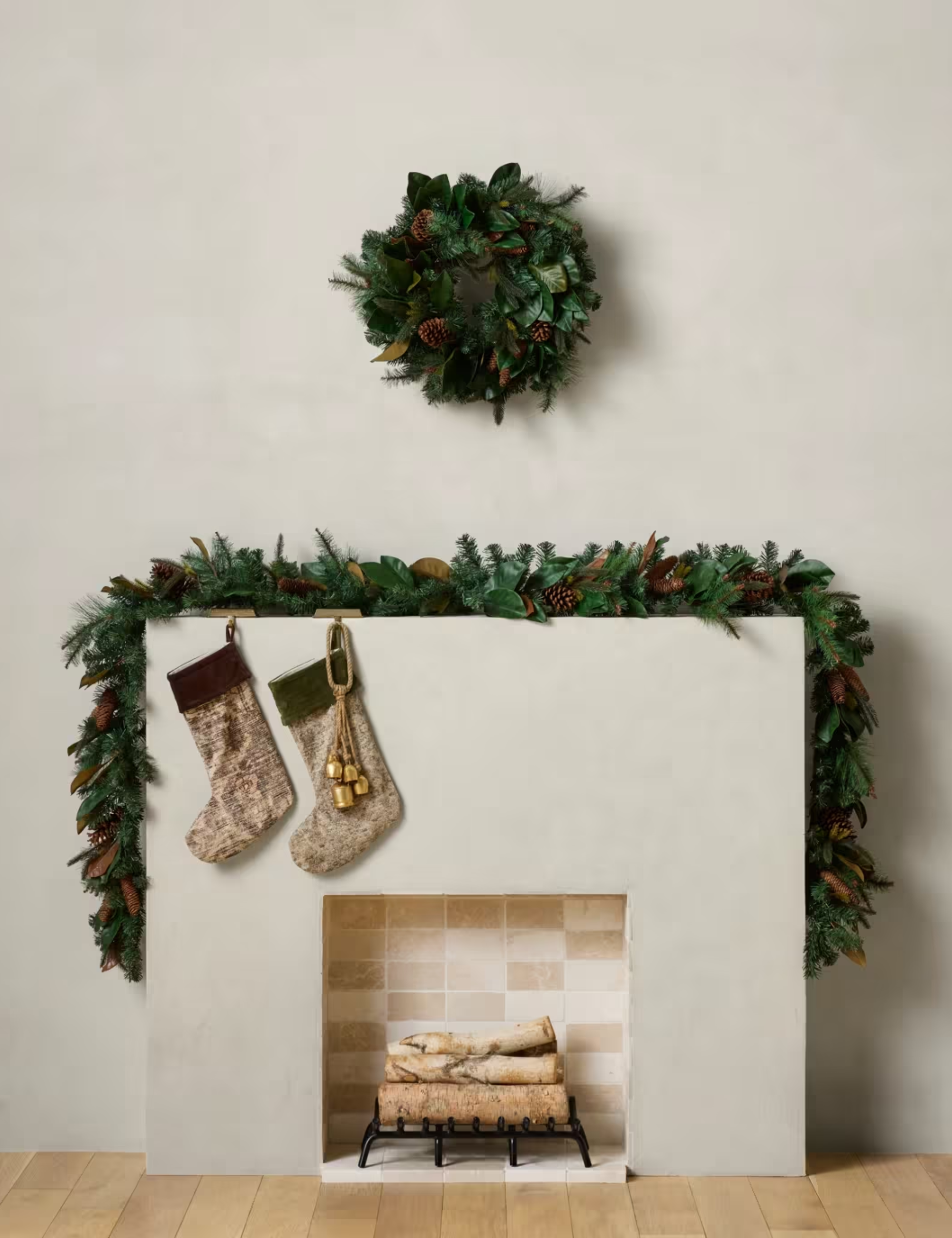 Fireplace mantel area styled with evergreen garland, a Christmas wreath, and two patterned stockings.