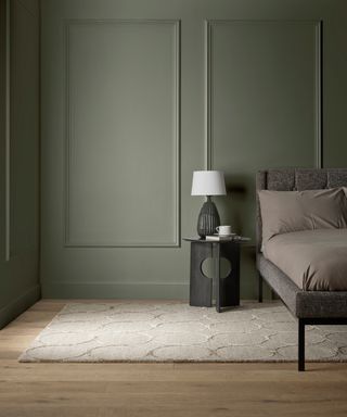 bedroom with sage green panelled walls, cream tufted rug with circular pattern and wooden flooring