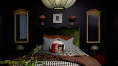 A dark dimly lit bedroom with symmetry in mirrors, side tables, desk lamps, and orange wall sconces