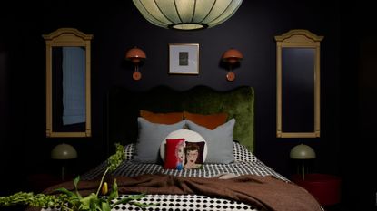 A dark dimly lit bedroom with symmetry in mirrors, side tables, desk lamps, and orange wall sconces