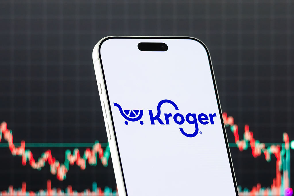 Kroger logo displayed on a smartphone screen with a stock market chart in the background