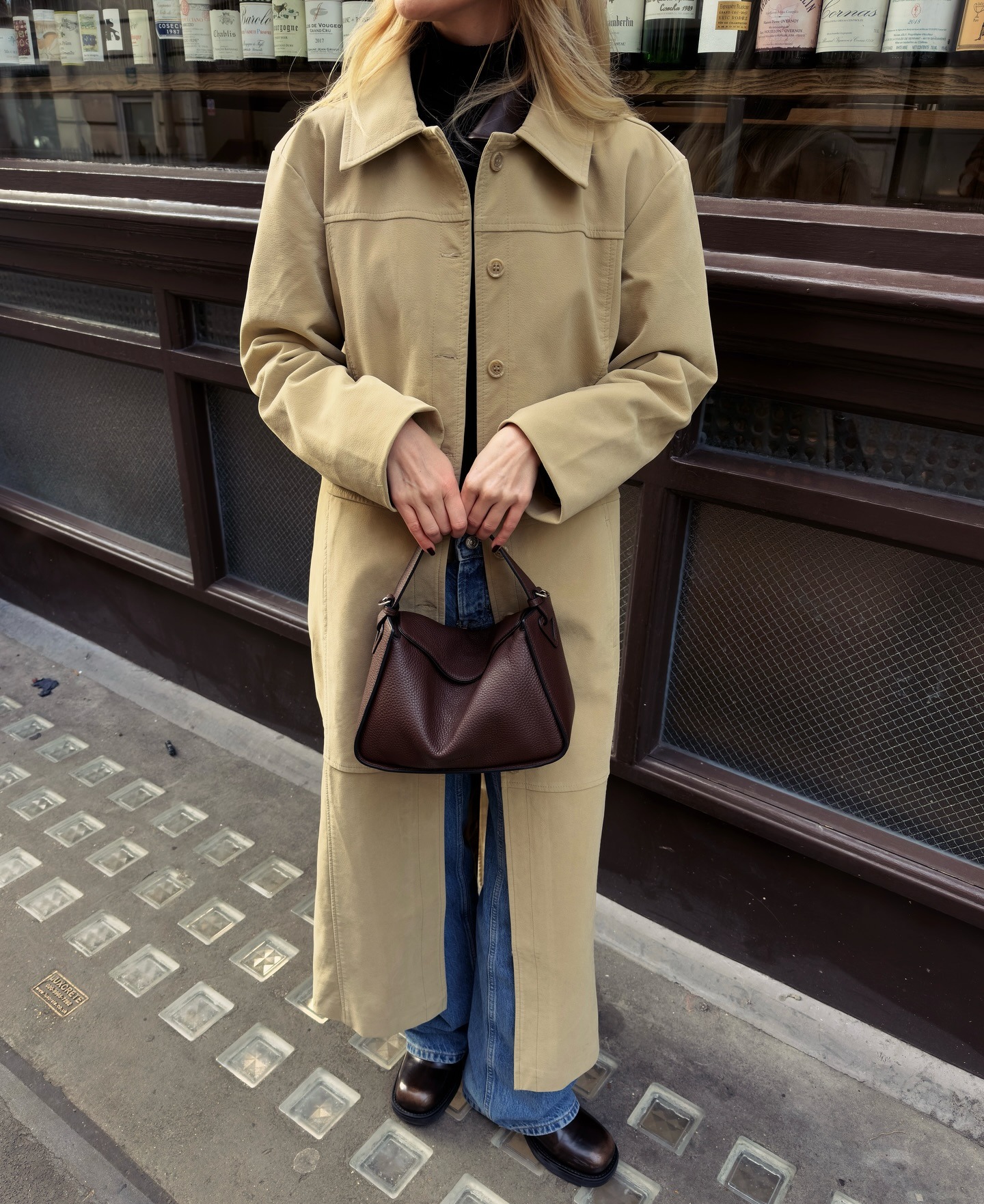 Woman wears beige long coat, blue jeans and carries The Horse Clementine bag