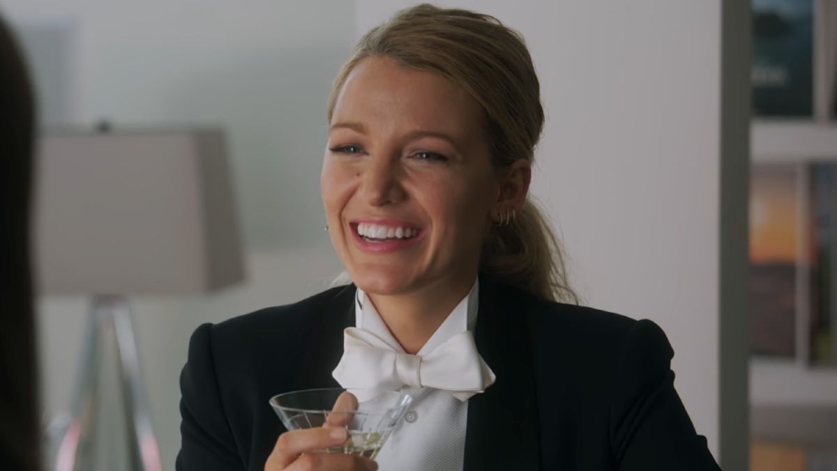 Blake Lively smiling while holding a martini glass and wearing a tux in A Simple Favor. 