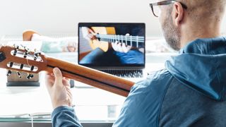 Man with acoustic guitar watches a lesson on his laptop