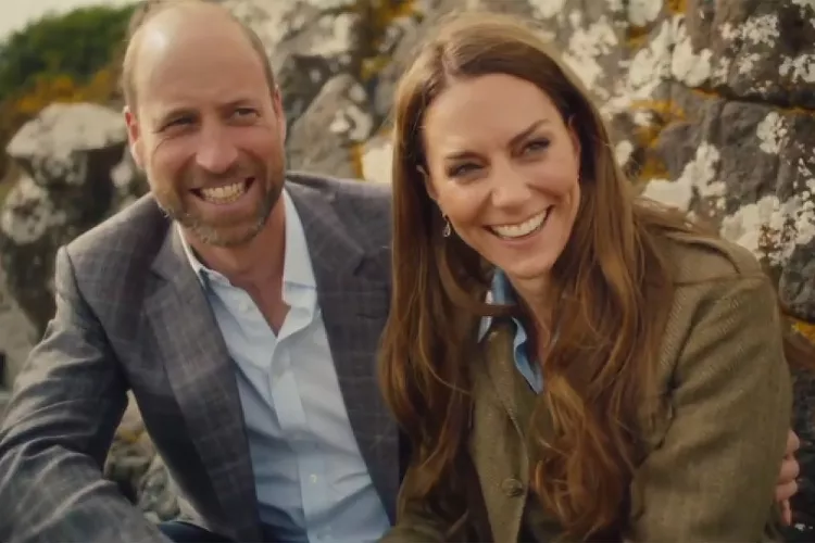 Prince William and Kate Middleton smiling wearing blazers sitting against a rock