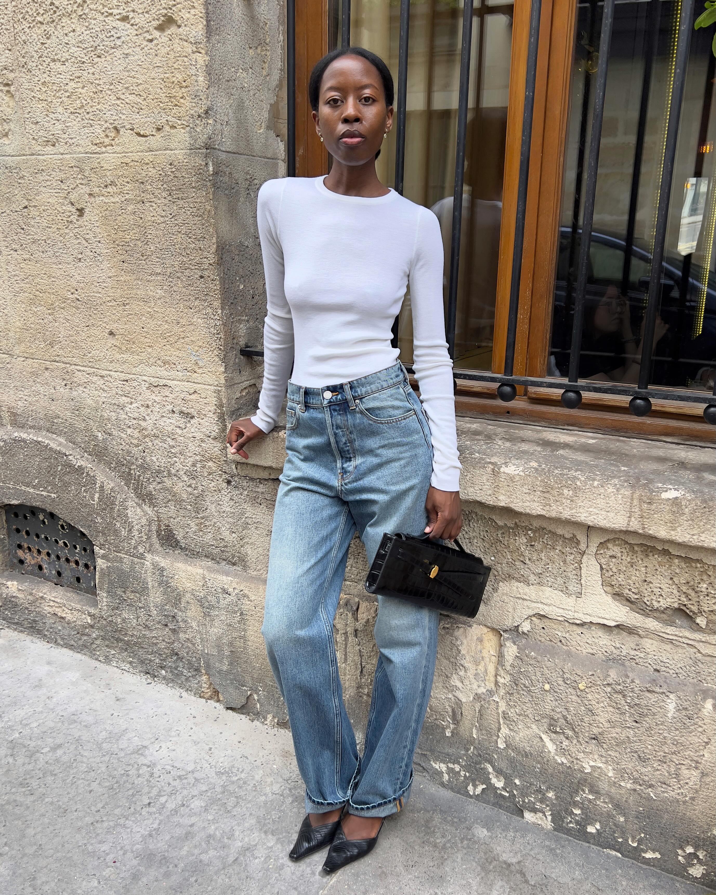 An image of an influencer wearing a white long-sleeve shirt, medium wash blue jeans and black kitten heels carrying a baguette bag in France
