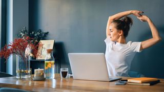 Woman stretching at home desk with laptop in front