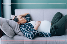 pregnant women lying on a sofa with her hand on her head looking thoughtful 