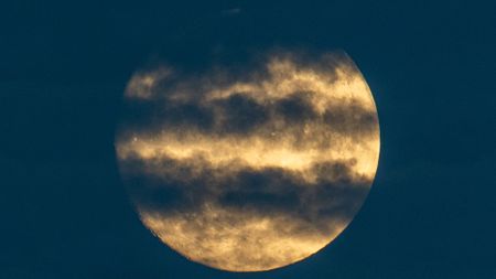 A yellow full moon glows in a dark sky with streaks of cloud lining its disk.