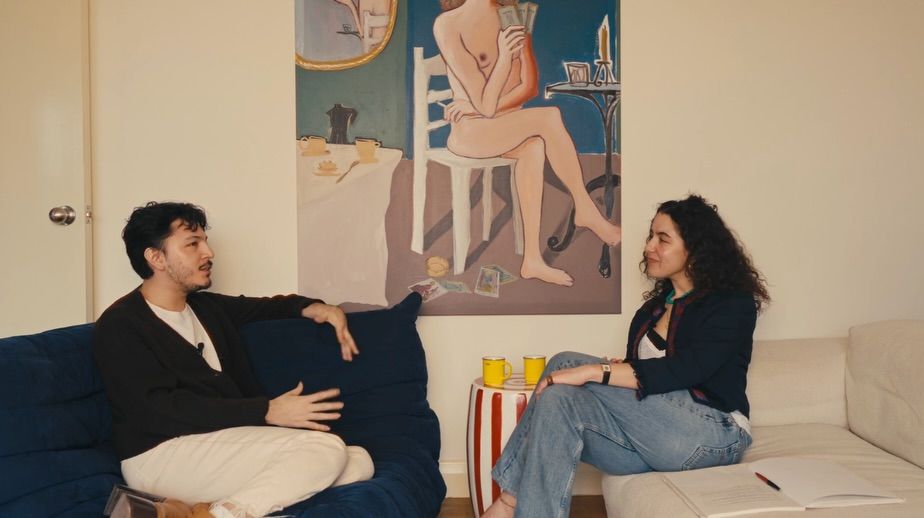 The interior of a young, brunette, curly-haired woman's living room-cum-kitchen, designed with pops of unexpected color, unique artwork, and sculptural sofas in blue and cream.