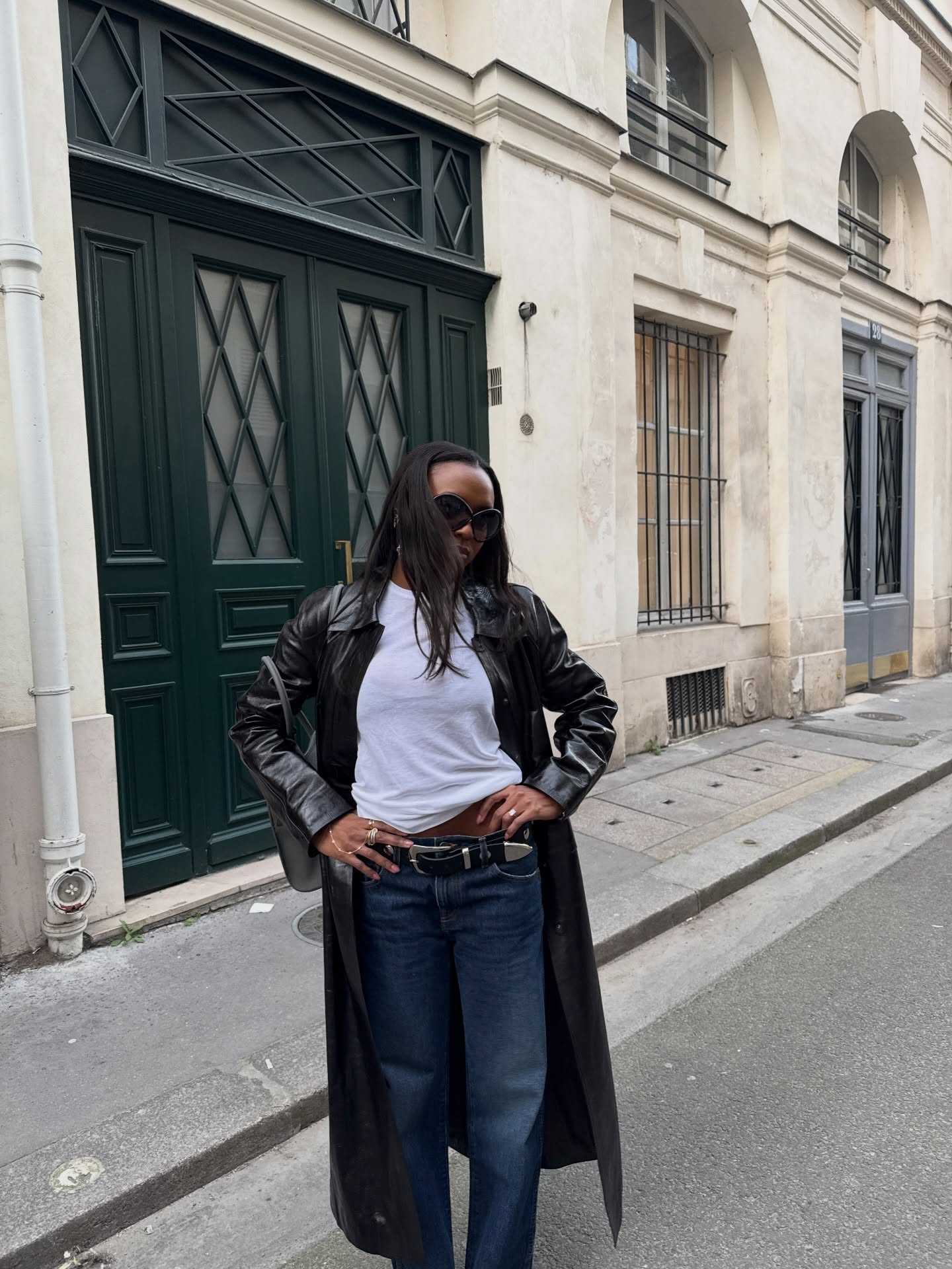 An image of an influencer in a black leather coat, white T-shirt and dark-wash jeans standing on a European street