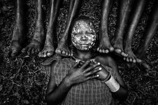 African woman lying on ground surrounded by bare feet of many others