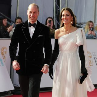 Prince William wearing a black tux walking the red carpet next to Kate wearing a white gown and black gloves