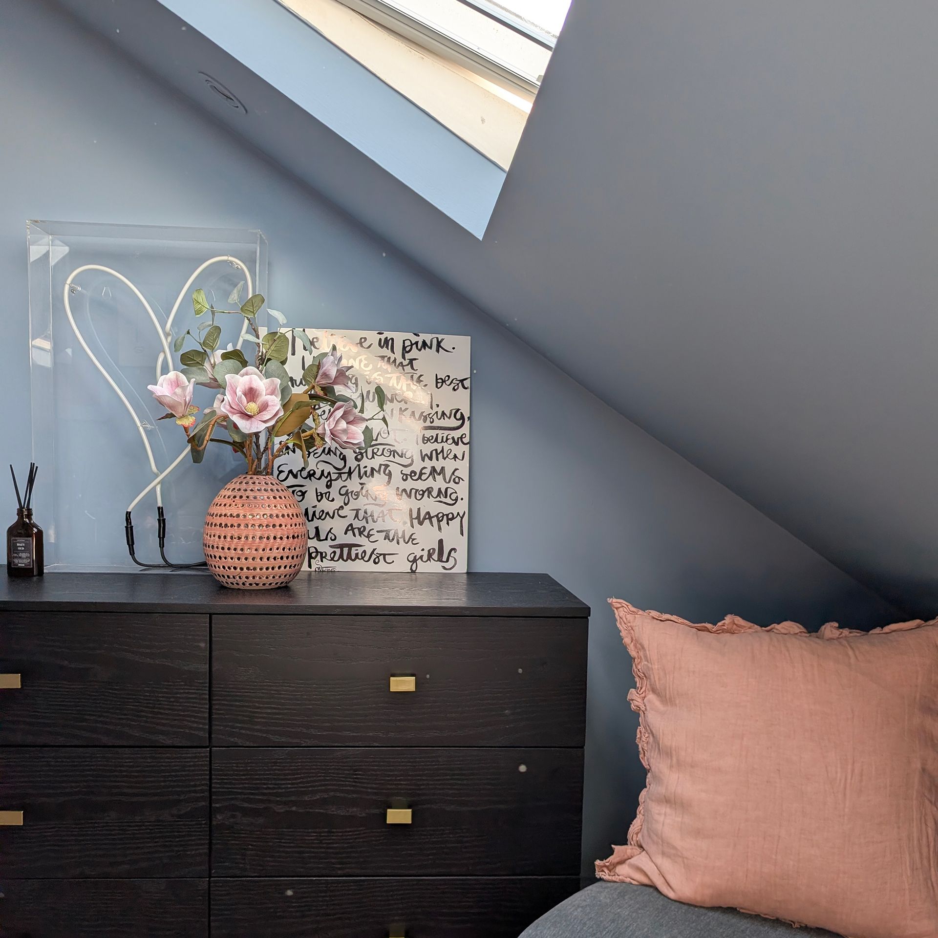 Colour drenched blue room with eaves and skylight above dark wood chest of drawers