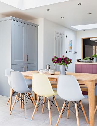 Light grey dining area with wooden table, blue and white chairs and blue cupboard