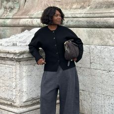Franny wears a black cardigan and grey tailored trousers from COS