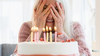 Senior woman peeking at candles on birthday cake.