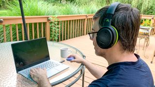 En skribent använder ett par Audeze Penrose-hörlurar medan han spelar på sin gaminglaptop ute på en veranda.