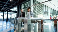 Two office workers walking into the lobby of their large, modern office building. Each is scanning their office card on their respective turnstile.