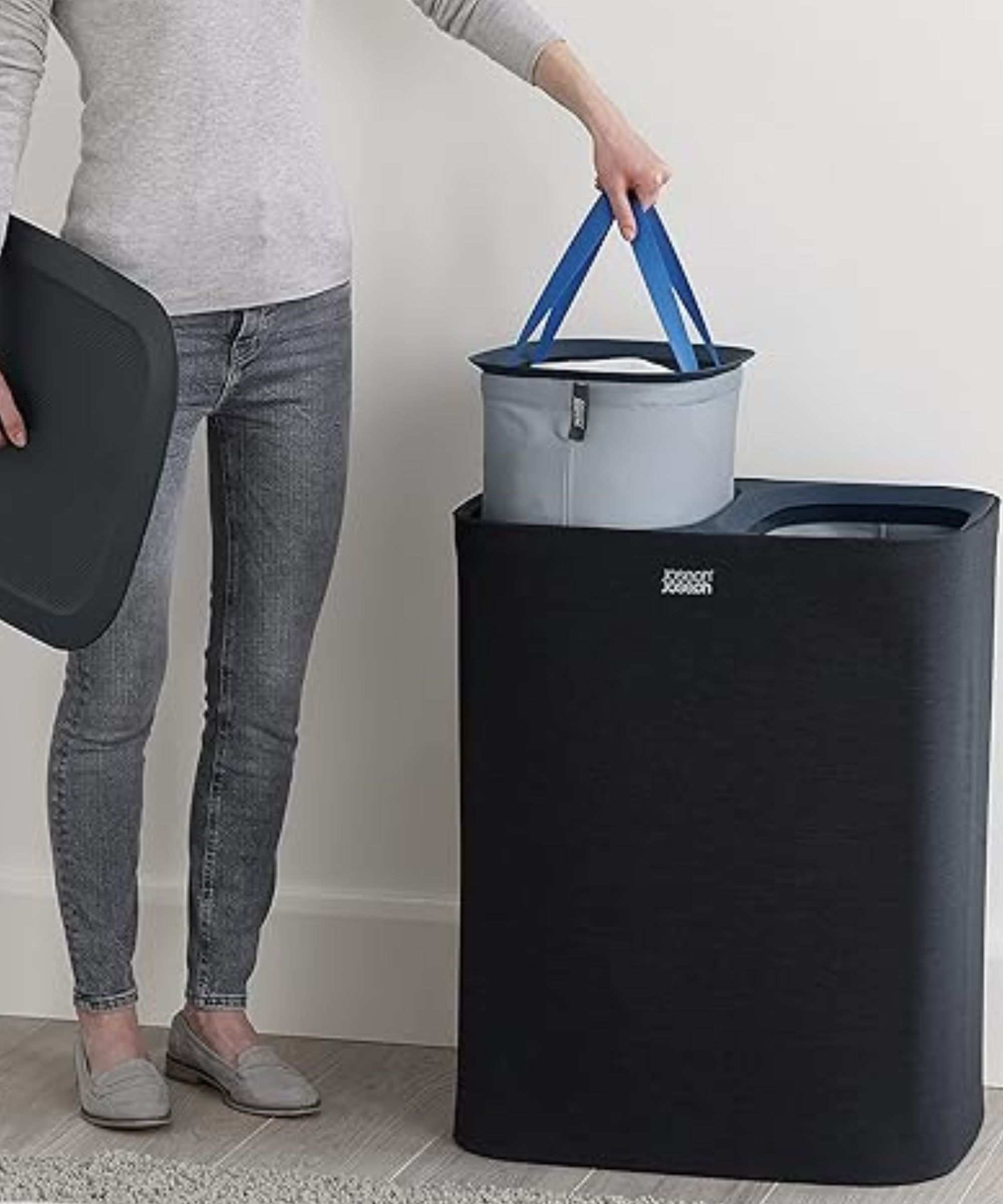 A person is pictured pulling one of the internal Joseph Joseph Tota laundry organizer bags out of its dark blue housing unit. She is holding the lid in her other hand.