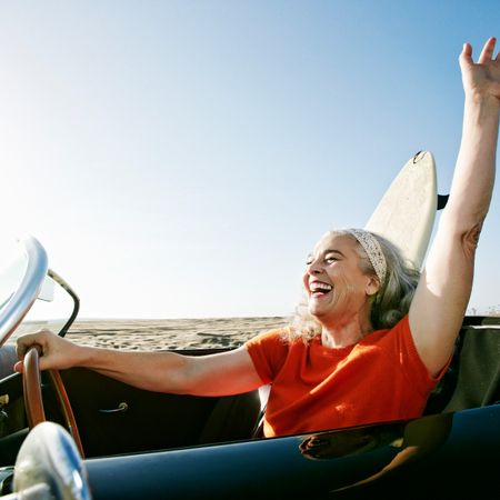 Woman arrives to beach in vintage car with surfboard in backseat.