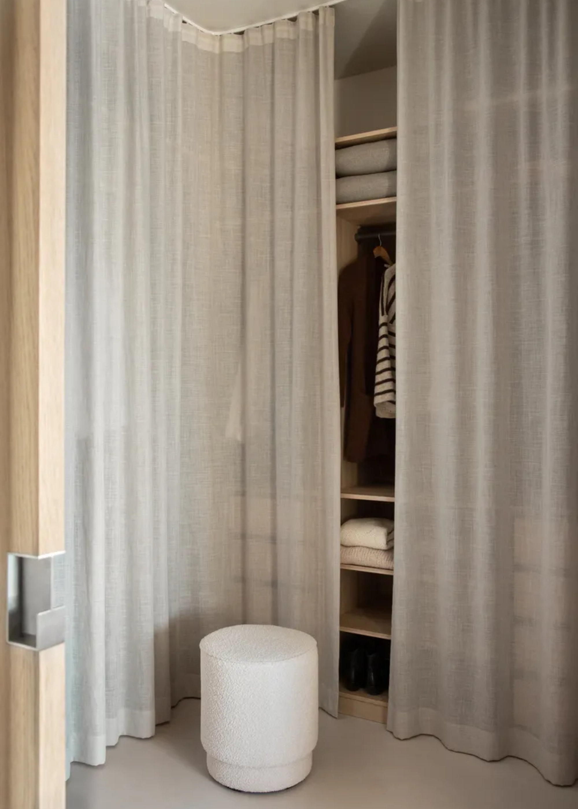An open wardrobe with a sheer curtain and a white pouf stool