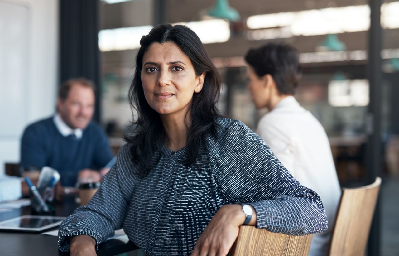 A Gen X woman in her forties turns from a business meeting to look at the camera.