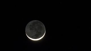 A new moon with a slim, illuminated crescent rises in a black sky