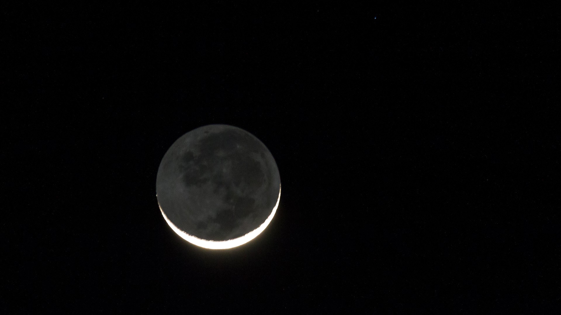 Uma lua nova fina e luminosa aparece acima de um céu negro